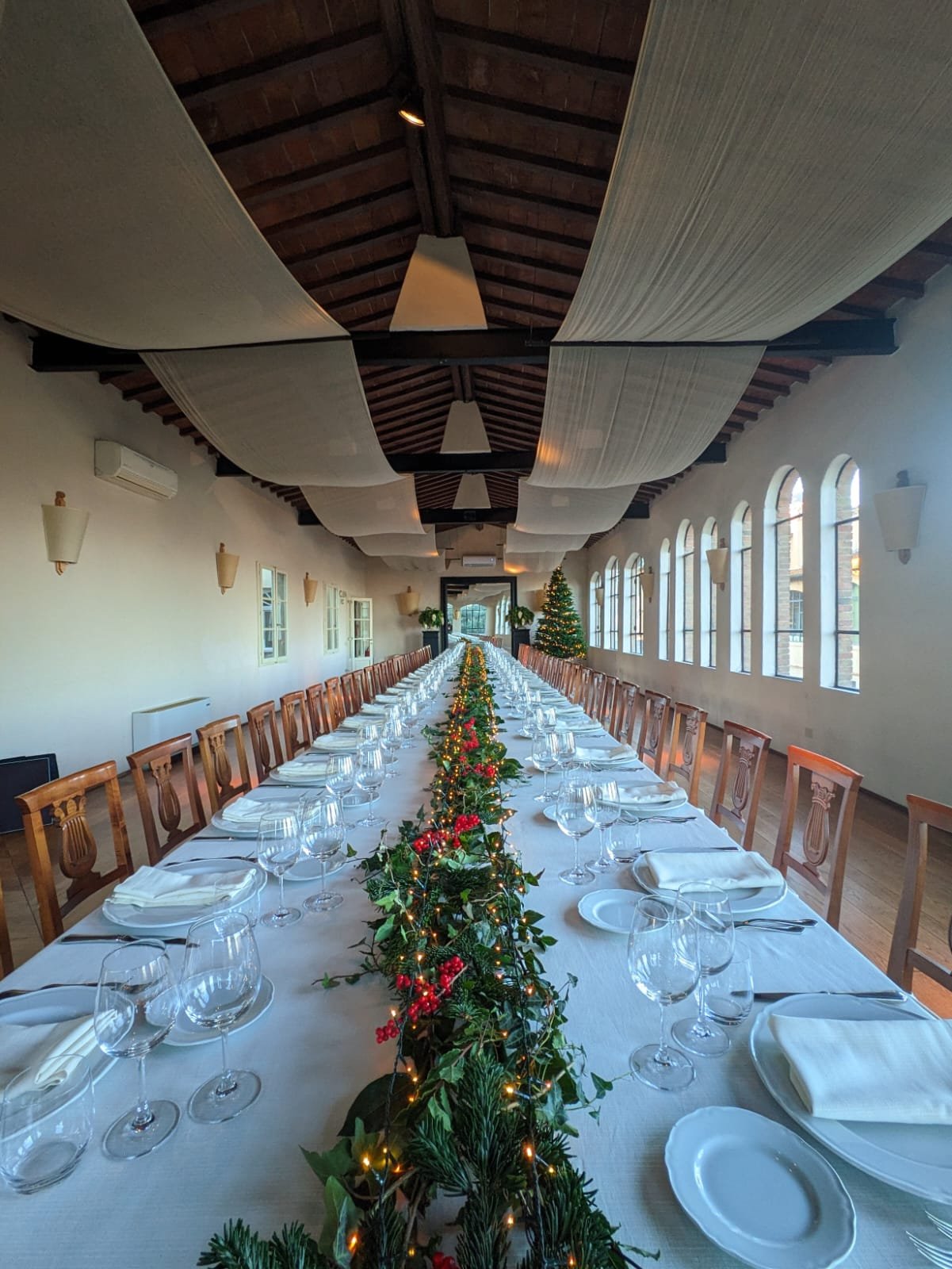 Lunga tavolata imbandita con ghirlanda natalizia e lucine, albero di Natale sullo sfondo, sala del Granaio di Villa Dianella
