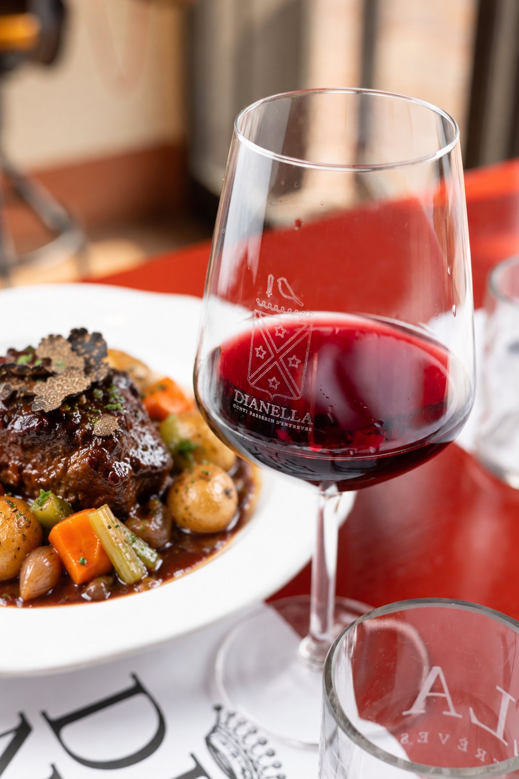 Guancia di manzo brasata al Chianti con lamelle di tartufo e verdure stufate, accanto a un calice di vino rosso Dianella
